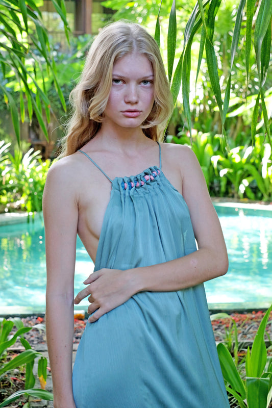 Close up front shot of young woman wearing a maxi length halter dress in yoryo chiffon featuring a pleated neckline with beads and adjustable neckties