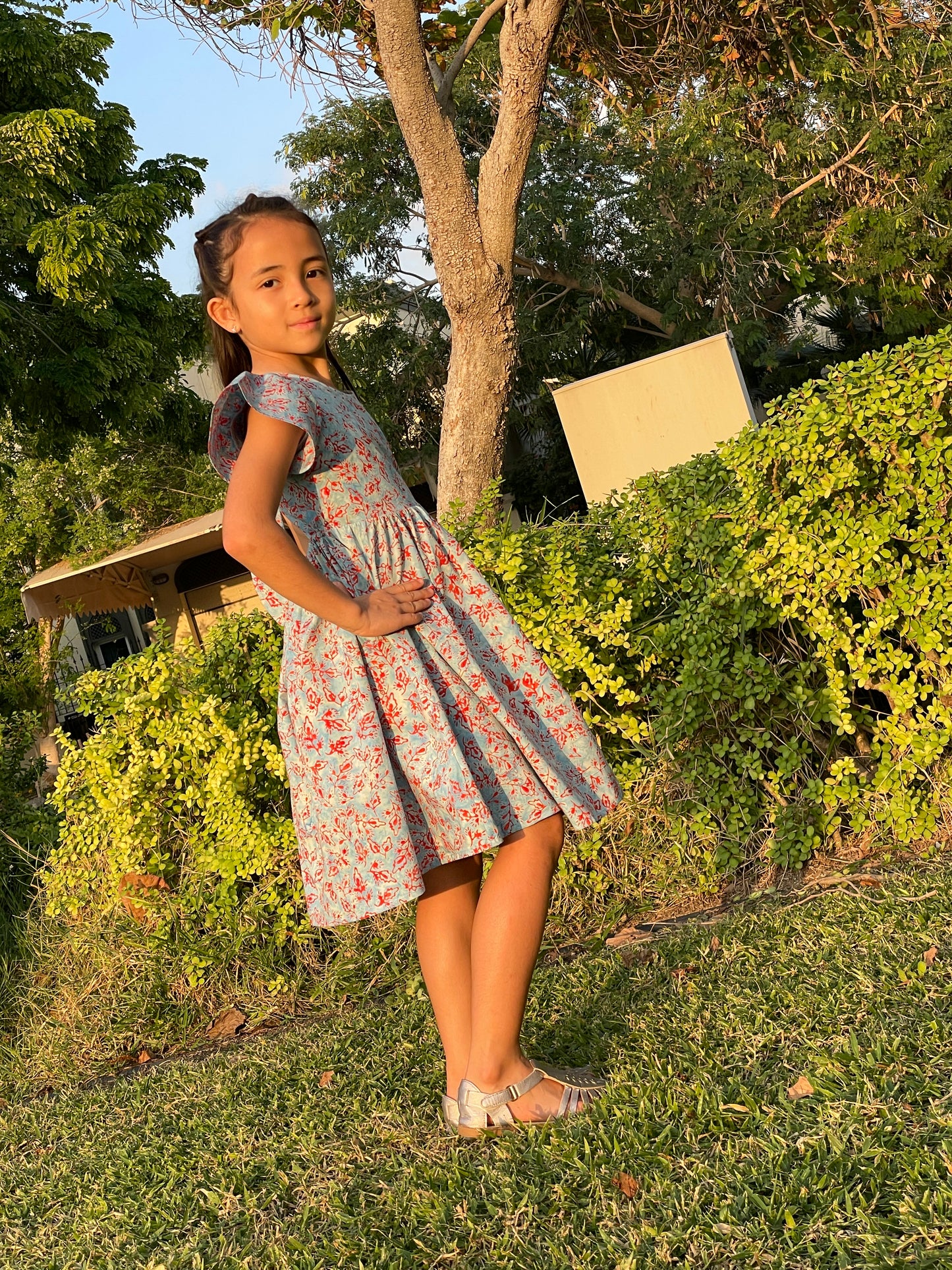 Side view of girl wearing a cotton batik dress in a blue and red floral print, showing the ruffle sleeves ad a-line of the dress, sustainably handmade in Bali, for sale in Dubai.