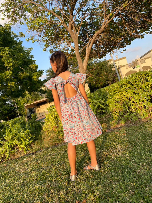 Back view of girl wearing a cotton batik dress in a blue and red floral print, showing the adjustable back ties and elastic waist of the dress, sustainably handmade in Bali, for sale in Dubai.
