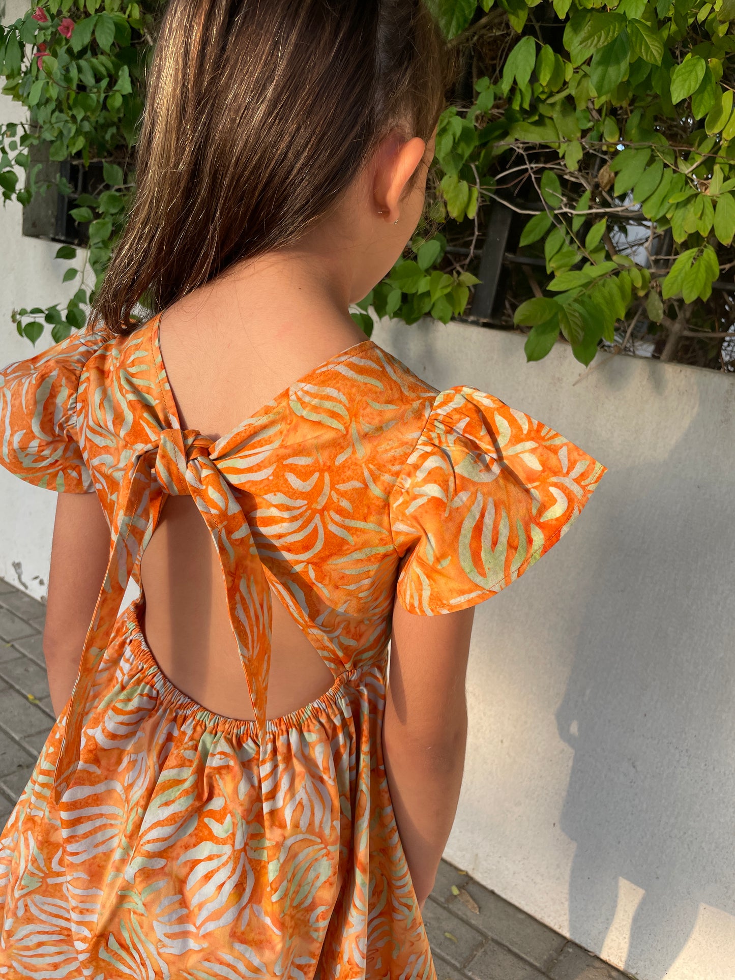 Back view of the Ivy orange tiger lily cotton batik dress, handmade sustainably in Bali by local artisans, featuring ruffle sleeves, adjustable back ties, and an a-line fit, perfect for outings in Dubai and those who love slow fashion style.