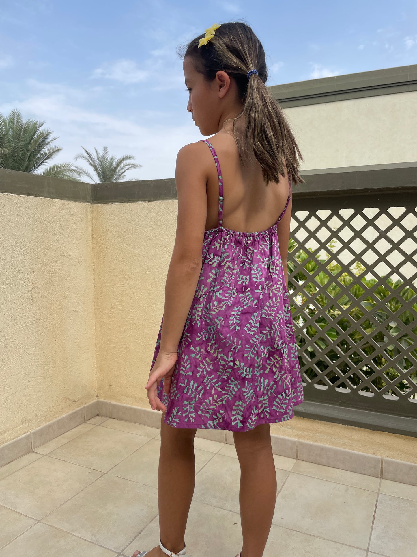 Back view of the Millie kids sundress handmade by artisans in Bali, featuring hand-stamped cotton batik in bright purple and aquamarine, with an a-line fit, adjustable waist band and spaghetti straps, for girls in Dubai