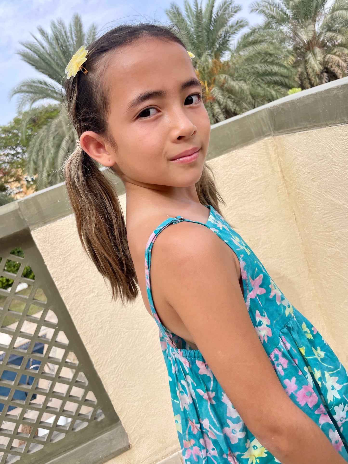 Close up front view of our Millie girls cotton dress made from green floral batik, artisan-made fabric from Indonesia, sustainably made fashion for girls in Dubai, featuring a-line fit, elastic waistband, and adjustable shoulder straps for perfect fit that grows with you child.