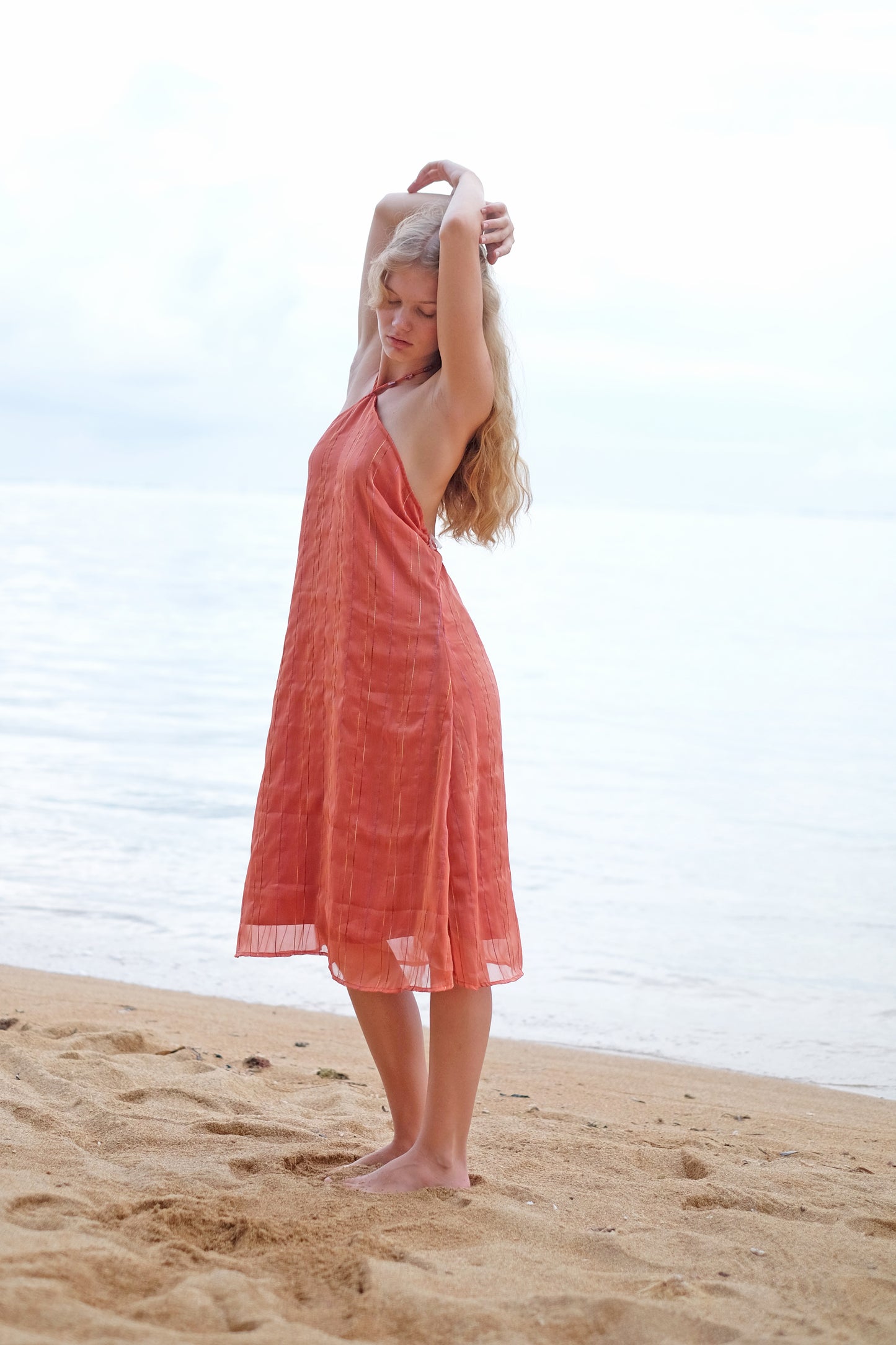 A side angle of the Mimi burnt orange midi dress, highlighting the halter neck and midi dress length, sustainable style made in Bali for women in Dubai.