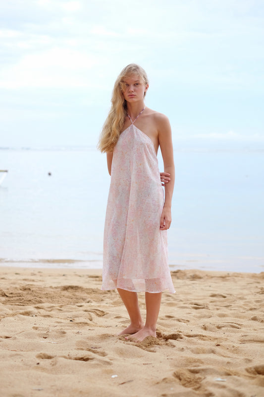 A front full length view of the Mimi midi halter dress in light pink floral print, showcasing its feminine design and flattering fit, sustainably made in Bali, perfect for adventures in Dubai