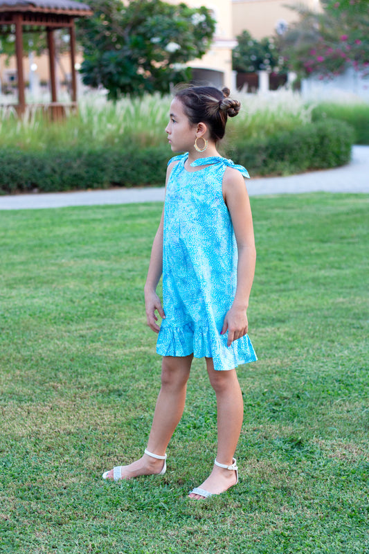 Side view of the Penelope Girls Batik Sundress in Blue Polka Dots. Hand-stamped batik, A-line silhouette, and adjustable ties. Perfect summer dress for girls in Dubai!