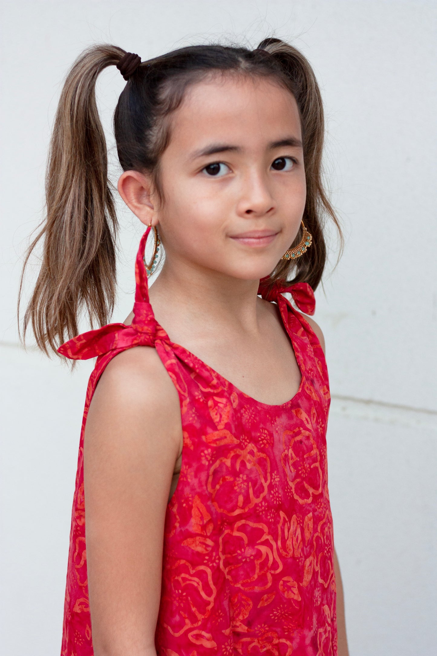 Close up view Penelope hand-stamped Indonesian cotton batik red knee-length a-line kids dress with adjustable rabbit ear shoulder ties and ruffle hem, perfect for fashionable little girls in Dubai, sustainably made in Bali