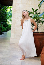 Load image into Gallery viewer, Young woman wearing a maxi length halter dress in textured white chiffon featuring a pleated neckline and backline with beads and adjustable neckties