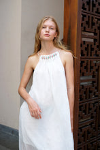 Load image into Gallery viewer, Young woman wearing a maxi length halter dress in textured white chiffon featuring a pleated neckline and backline with beads and adjustable neckties, for fashionistas loving handmade sustainable slow fashion brands