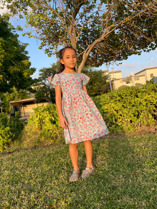 Full length front view of girl wearing a cotton batik dress in a blue and red floral print, sustainably handmade in Bali, for sale in Dubai.