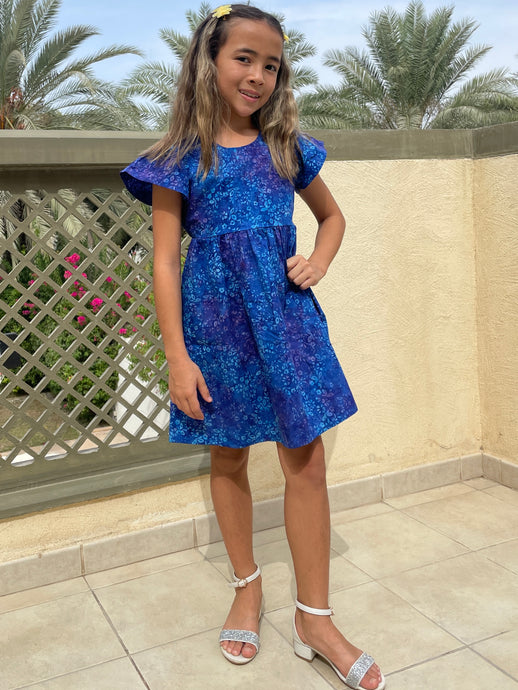 Front view of girl wearing a cotton batik dress in a contrasting blue floral print, showing the ruffle sleeves and a-line shape of the dress, sustainably handmade in Bali, for sale in Dubai.