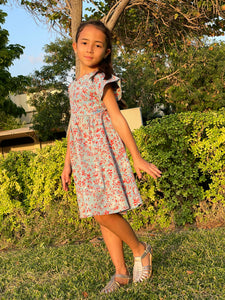 Front view of girl wearing a cotton batik dress in a blue and red floral print, showing the ruffle sleeves of the dress, sustainably handmade in Bali, for sale in Dubai.