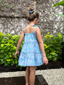 Girls sundress for kids made from blue and purple artisan-made batik cotton fabric, shown from the back view, also wearing fuchsia handmade moroccan style earrings, also wearing a scrunchie made from the same fabric as the dress for zero-waste, handmade fashion in Bali, for young fashionistas in Dubai