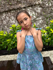 Close up view of girls sundress for kids made from blue and purple artisan-made batik cotton fabric, shown from the back view, also wearing fuchsia handmade moroccan style earrings, handmade fashion in Bali, for young fashionistas in Dubai