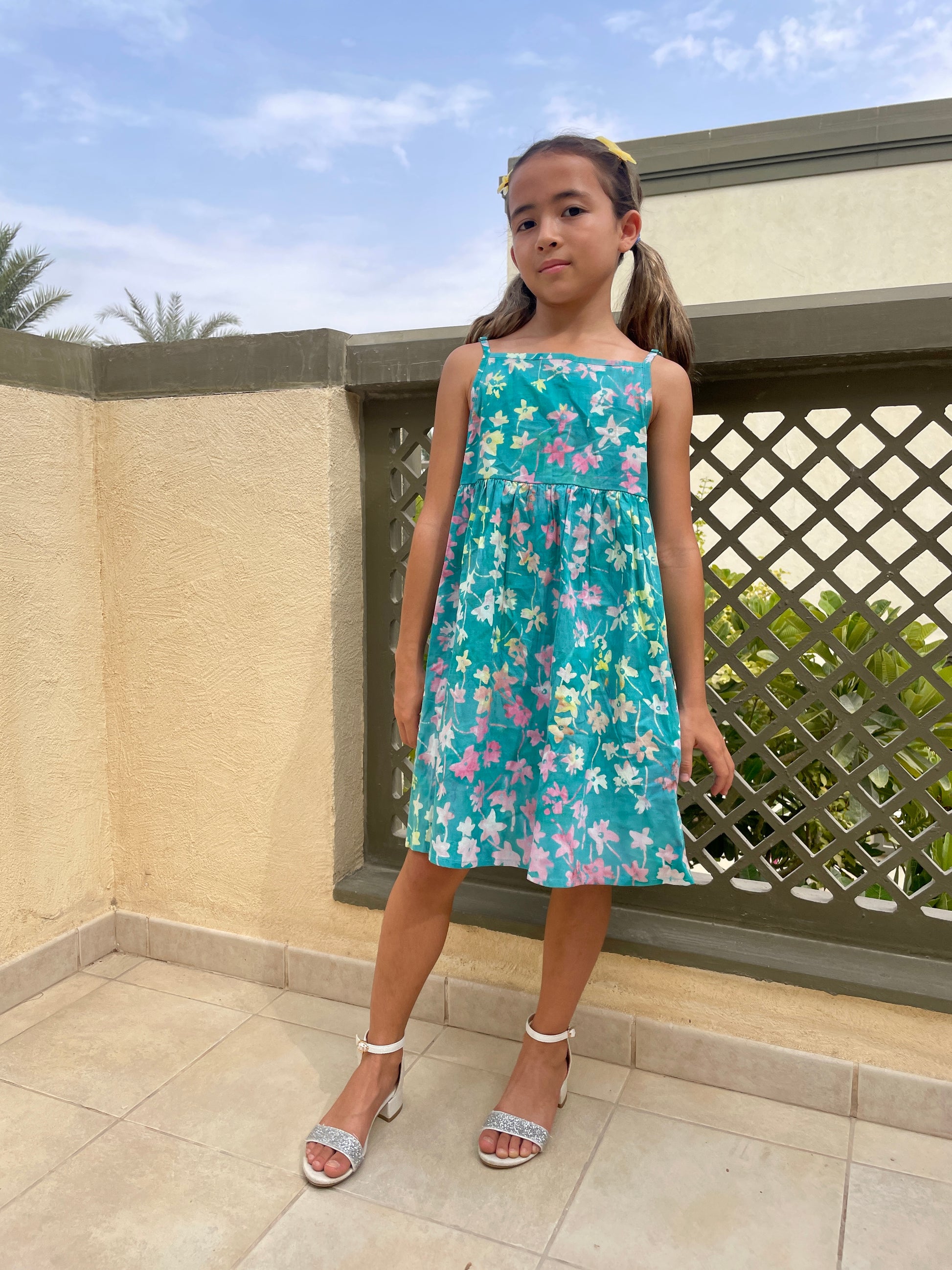 Front full length view of our Millie girls cotton dress made from green floral batik, artisan-made fabric from Indonesia, sustainably made fashion for girls in Dubai, featuring a-line fit, elastic waistband, and adjustable shoulder straps for a perfect fit that grows with you child.
