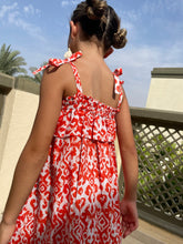 Load image into Gallery viewer, Close up shot of Indonesian hand-stamped orange ikat print cotton batik dress for girls in Dubai, ruffles and adjustable shoulder ties, knee length, sustainably made in Bali, paired with cream tassel earrings