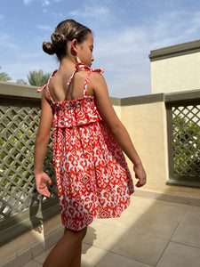 Close up back shot of Indonesian hand-stamped orange ikat print cotton batik dress for girls in Dubai, ruffles and adjustable shoulder ties, knee length, sustainably made in Bali, paired with cream tassel earrings
