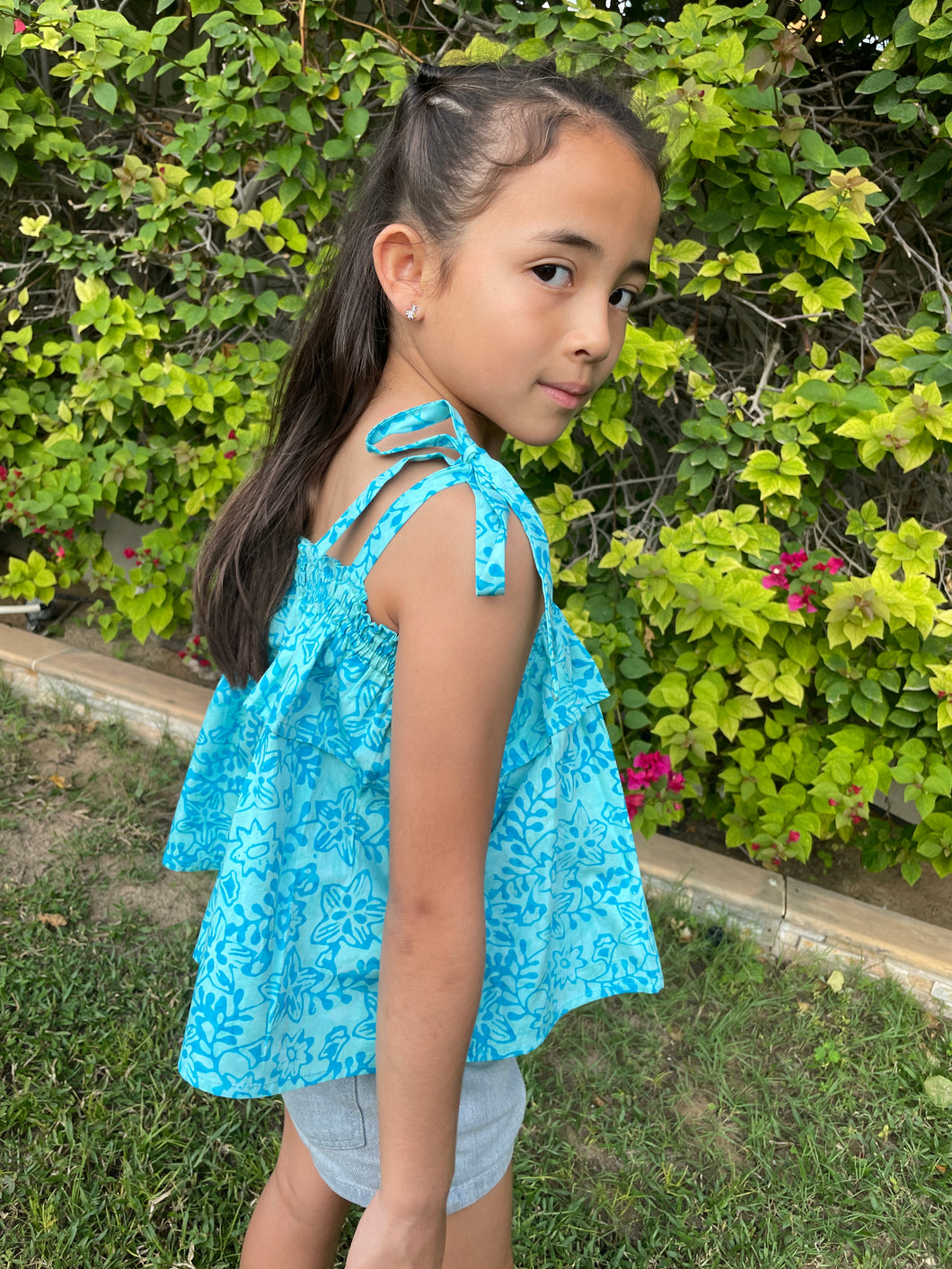Close up photo of girl wearing light blue floral cotton batik top, with ruffles along neck and backlines, adjustable shoulder ties, can also be worn as skirt, handmade by artisans in Bali, available in Dubai