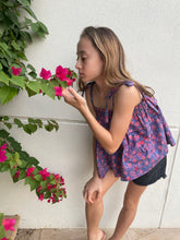 Load image into Gallery viewer, Side view close up of girl wearing purple ruffle top with shoulder ties and black shorts, the top is made from Indonesian cotton batik, available in Dubai