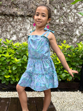 Load image into Gallery viewer, Front view of girls sundress for kids made from blue and purple artisan-made batik cotton fabric, also wearing fuchsia handmade moroccan style earrings, handmade fashion in Bali, for young fashionistas in Dubai