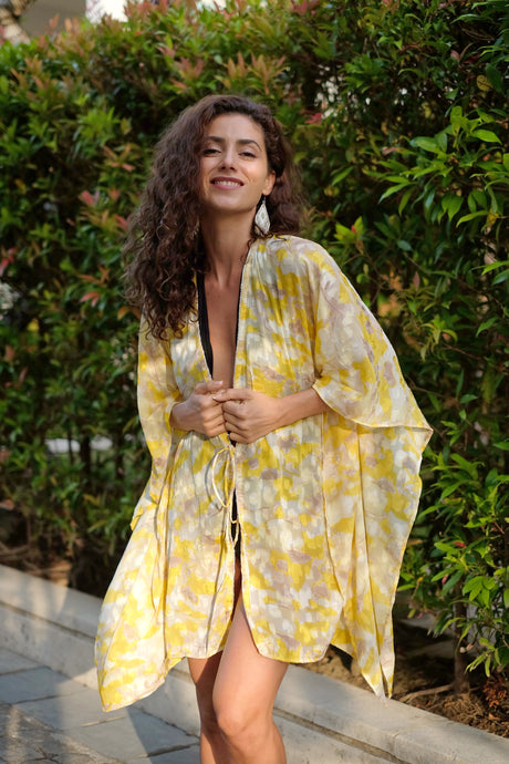 A boho glamorous textured vibrant yellow, white, and gray women's beach kaftan with rhinestone trimmed neckline and handmade beaded earrings, designed in Dubai, handmade in Bali
