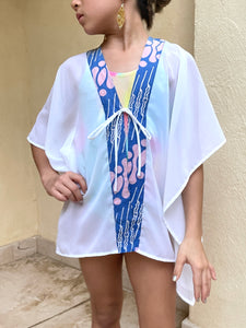 Onism kids kaftan in white lurex chiffon with vibrant pink and blue batik trim, perfect for beach days in the UAE.
