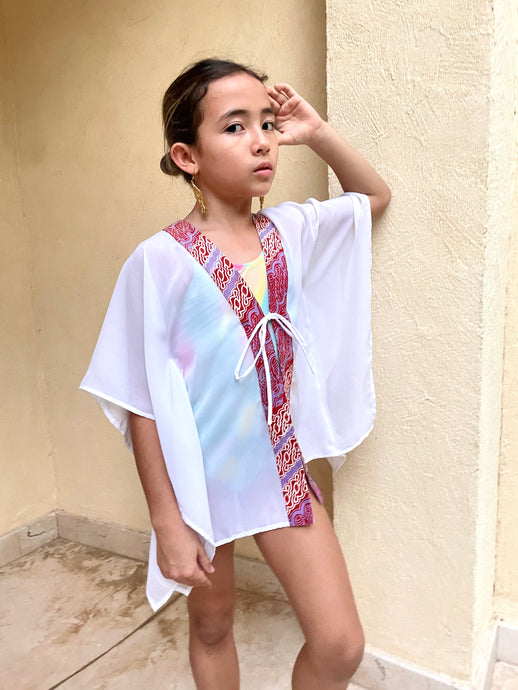 Onism Kids Beach Kaftan, sustainably handmade in Bali, with shimmering white lurex chiffon and bold purple and burnt orange batik trim.
