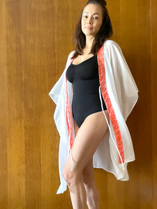 Flowy and chic white kaftan with orange floral batik trim – perfect for tropical getaways
